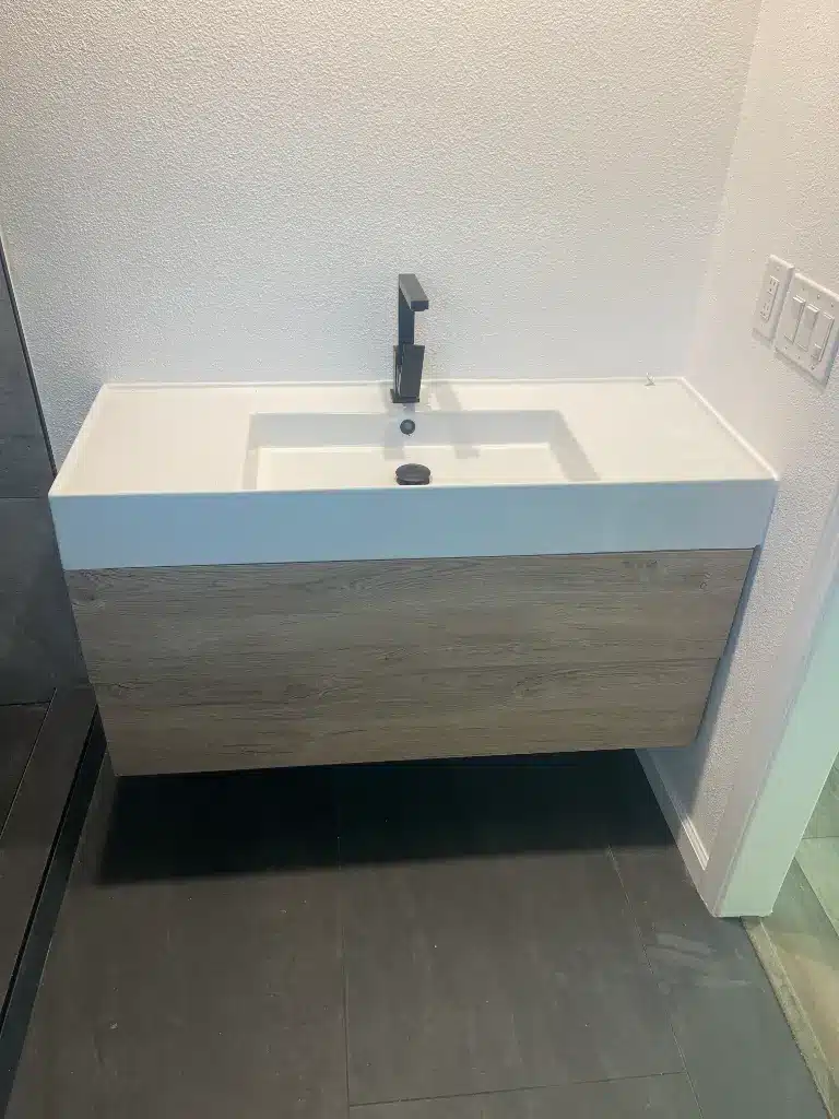 Floating bathroom vanity with a wide rectangular sink and matte black faucet against a textured white wall.