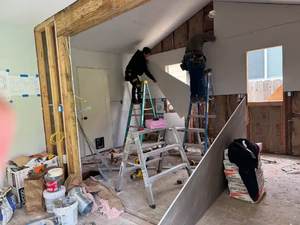 Two construction workers installing drywall on an interior wall during a home renovation project.
