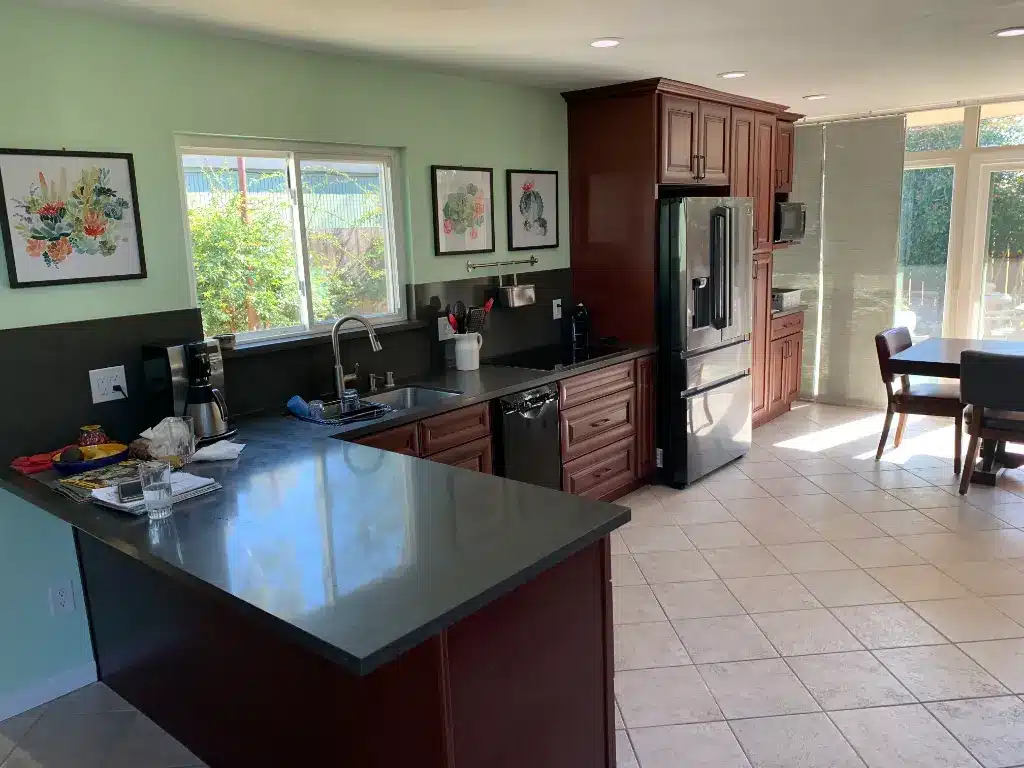 Modern kitchen with dark countertops, cherry cabinets, stainless appliances, and a small dining area by large windows