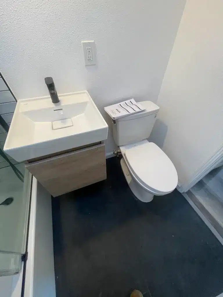 Small floating vanity with a rectangular sink beside a white toilet and dark tile flooring.