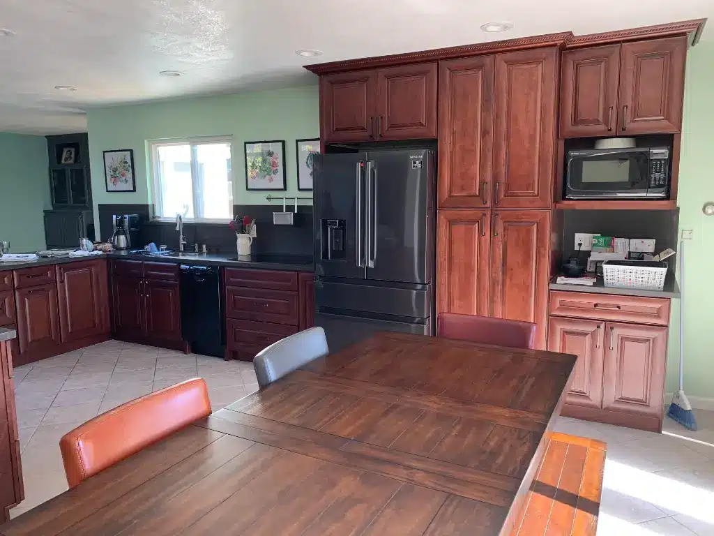 Updated kitchen with cherry cabinets, black appliances, dark countertops, and a wooden dining table in natural light